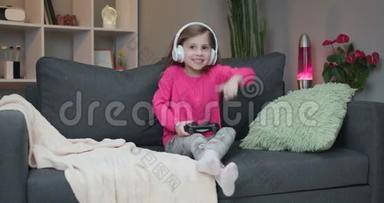 年轻的小女孩坐在沙发上在家里的客厅里播放视频。 兴奋的玩家女孩手拿操纵杆